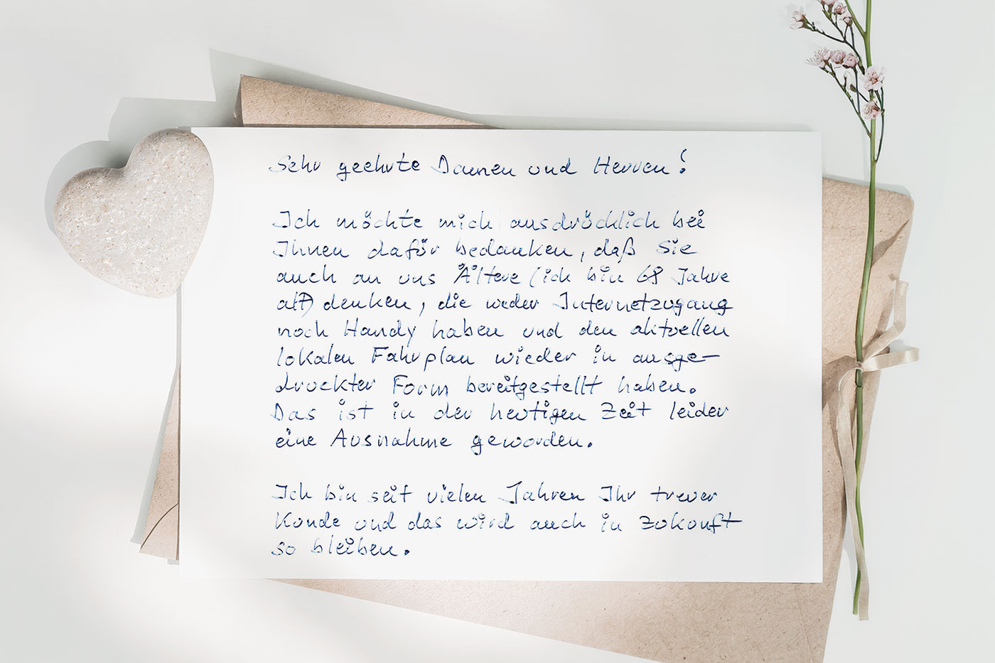 Handgeschriebener Brief mit einem kleinen Herz aus Stein und einer dezenten Blume und einem hellbraunen Umschlag.