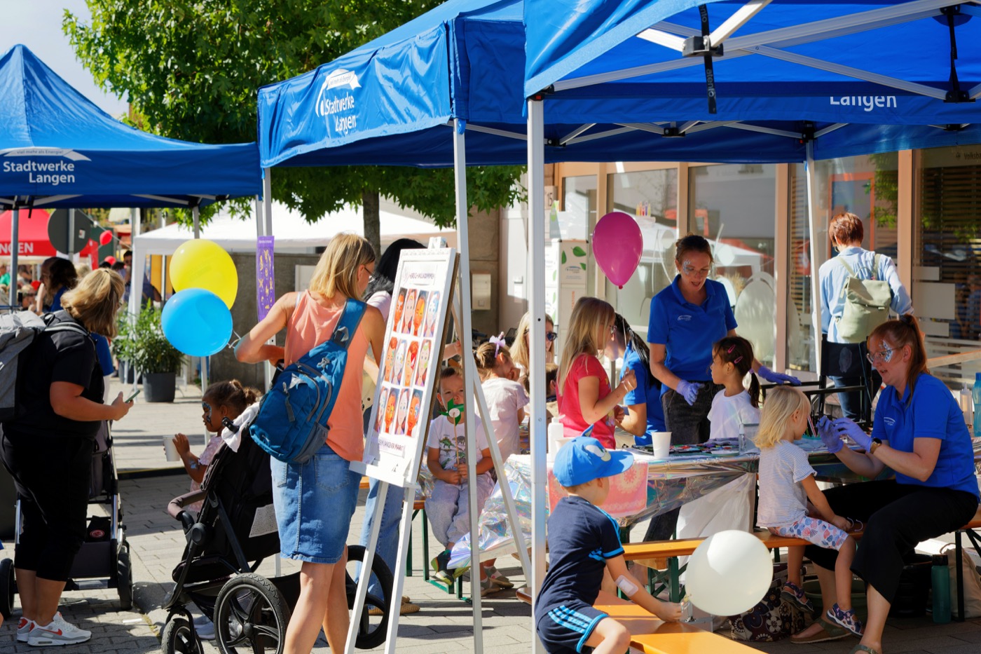 Der Stand der Stadtwerke Langen mit mehreren Kindern, Erwachsenen und den Mitarbeiterinnen die Kinder schminken.