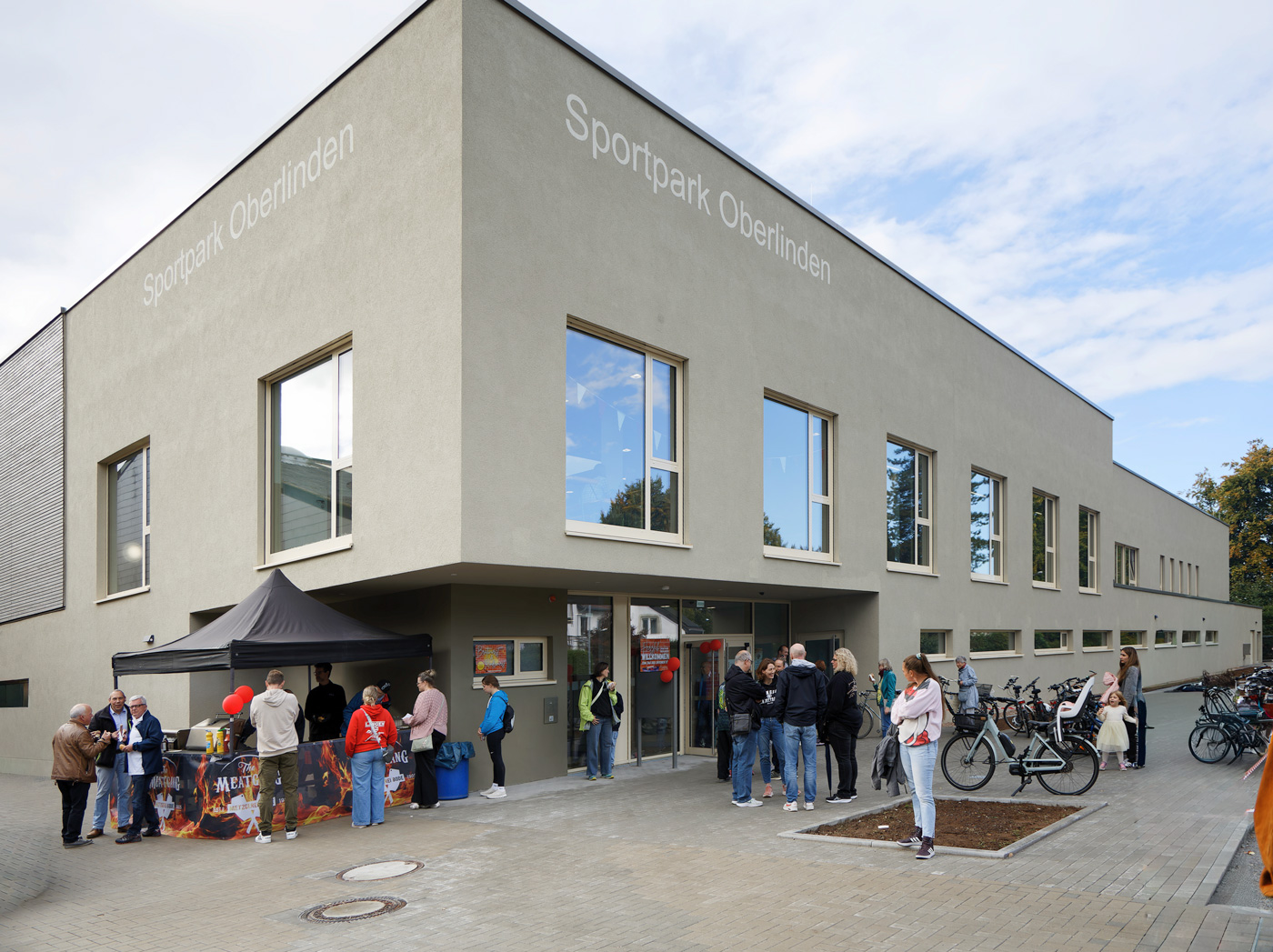 Eingang der Vier-Felder-Halle mit einem Grill-Zelt, mehreren Personen und Luftballons zur Eröffnung.