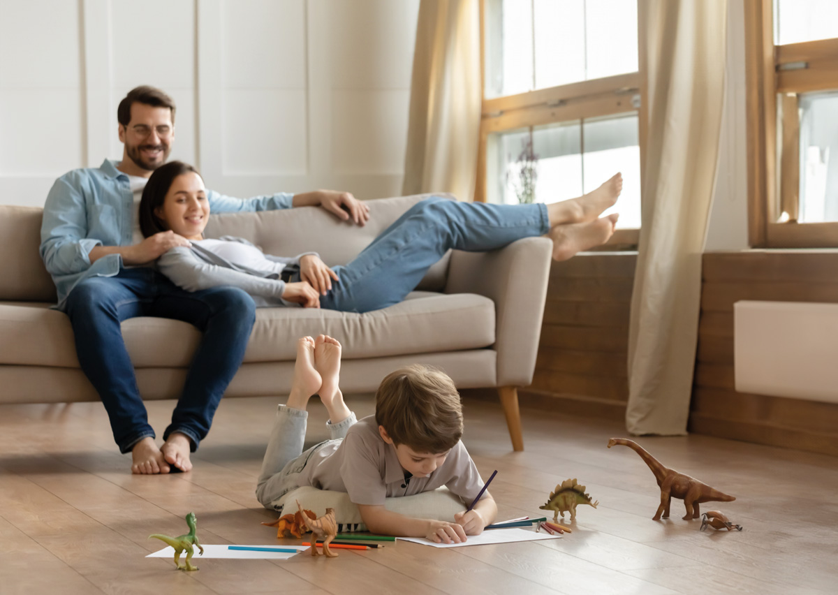 Frau und Mann sitzen auf Sofa und schauen dem spielenden Kind zu
