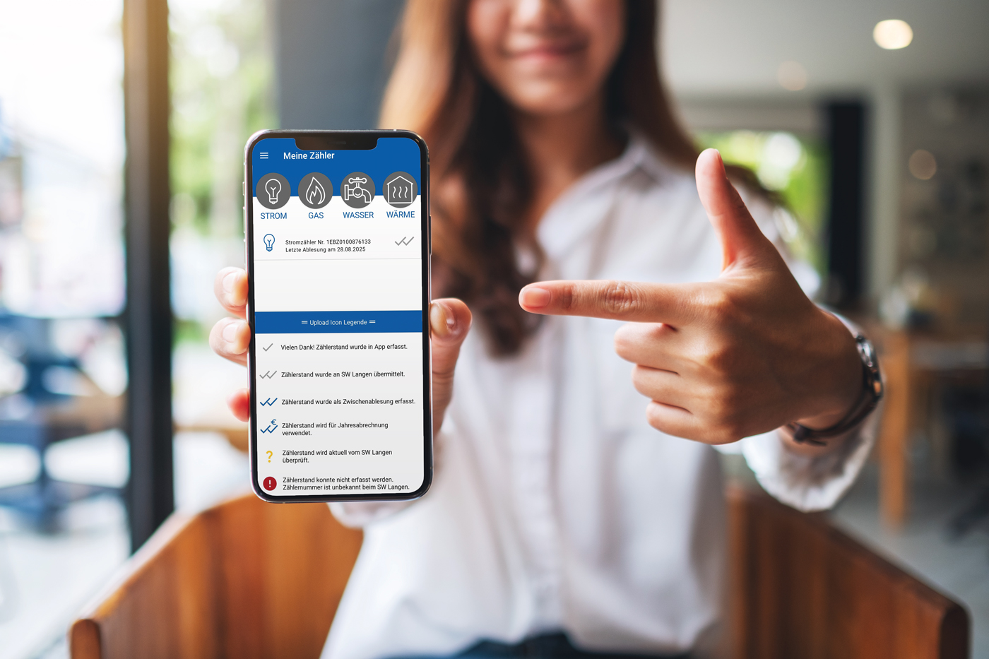 Junge Frau hält Smartphone mit Abbildung der Zusamme-Fix-App in die Kamera und zeigt mit dem Finger der anderen Hand darauf.